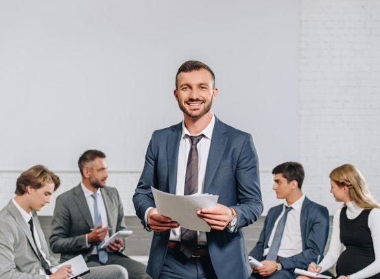 happy business coach standing in front of businesspeople at training in hub